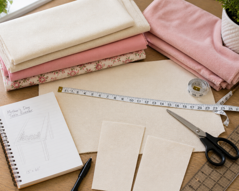 Mother’s Day fabric yardage planning scene with folded fabric, measuring tape, scissors, and project pieces for sewing gifts and decor