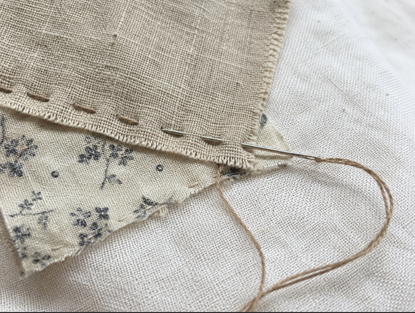 Close-up of running stitch attaching layered fabric scraps to a cotton base for slow stitching
