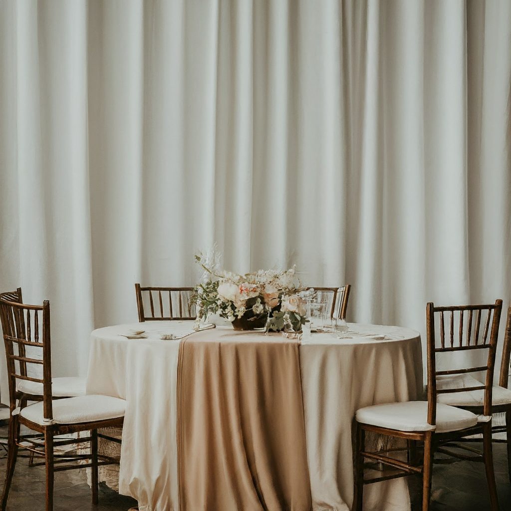 A wedding reception with elegant white pipe and drape backdrop